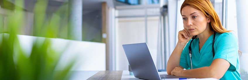 Focused female CCMA working on laptop in modern hospital