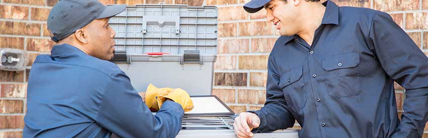 HVAC technicians working together on AC unit