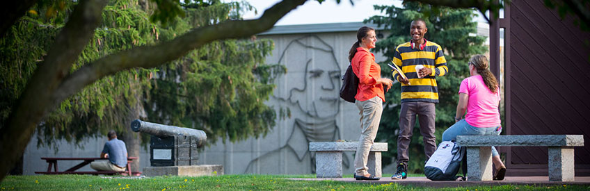 Three students smiling at benches on campus on a bright summer day. 