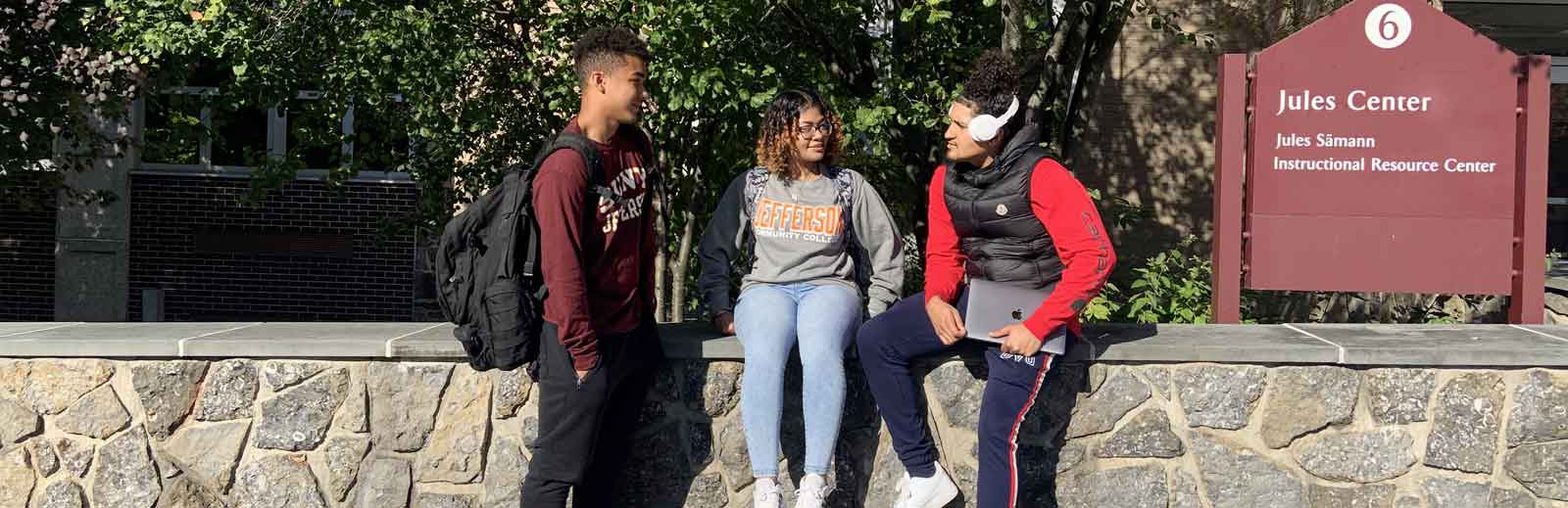 3 Students sitting in front of Jules Center on Campus