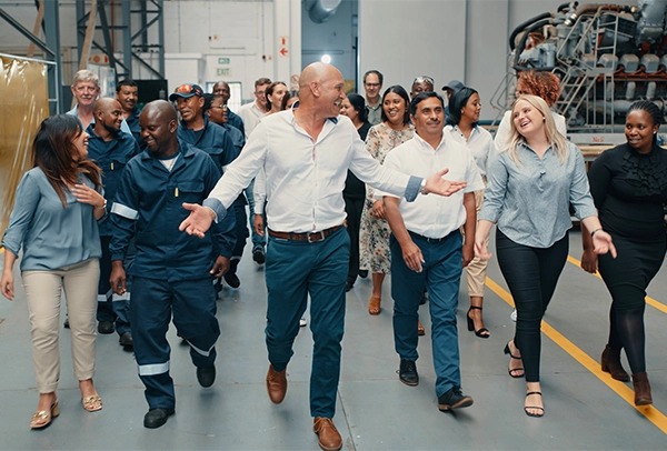 Happy, excited and smiling workers walking around modern industrial warehouse with manager or ceo leading employees. Group, team or coworkers taking a tour and learning logistics with leadership.