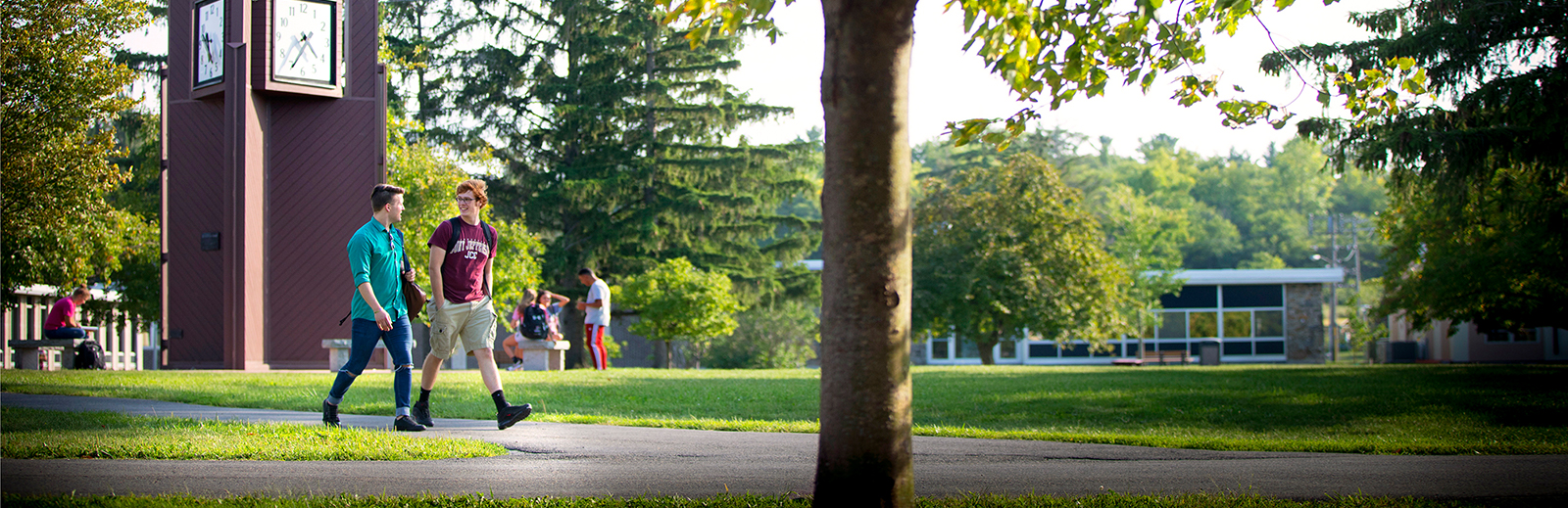 Two students talking and walking through campus. Students in the background talking near the clock tower.